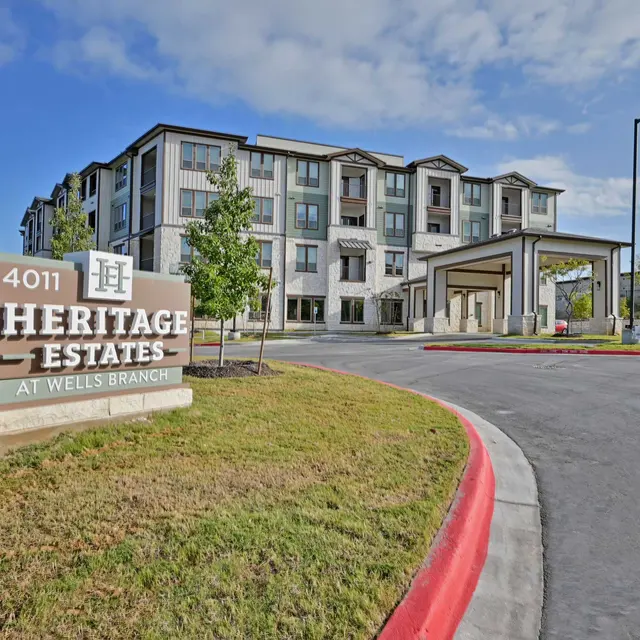Entrance of Heritage Estates at Wells Branch, showcasing a modern multi-story building and a welcoming sign.