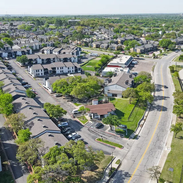 Aerial view of a residential neighborhood featuring apartment buildings, a road, and greenery surrounding the area.