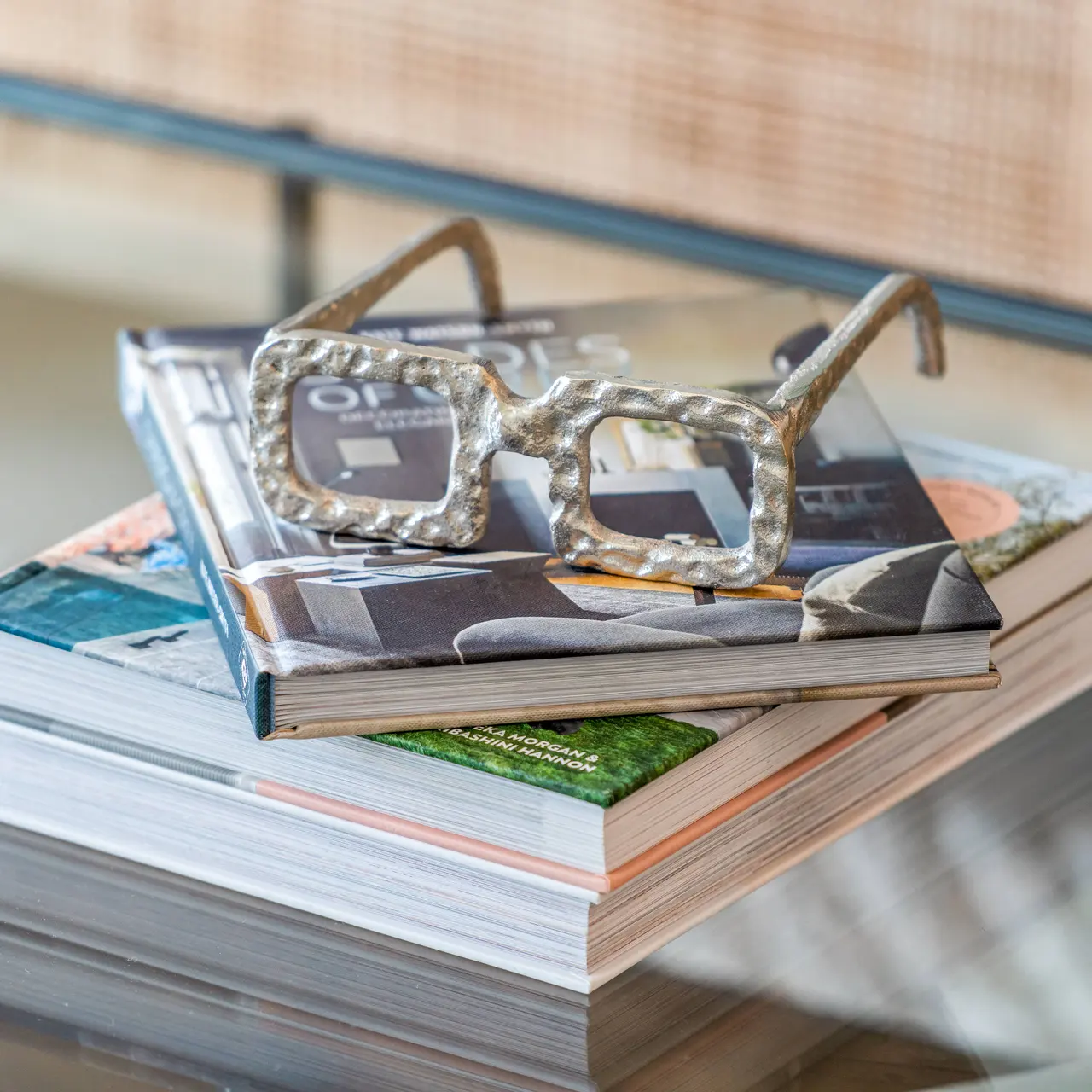 A pair of stylish clear-framed glasses resting on top of two neatly stacked books on a glass table.
