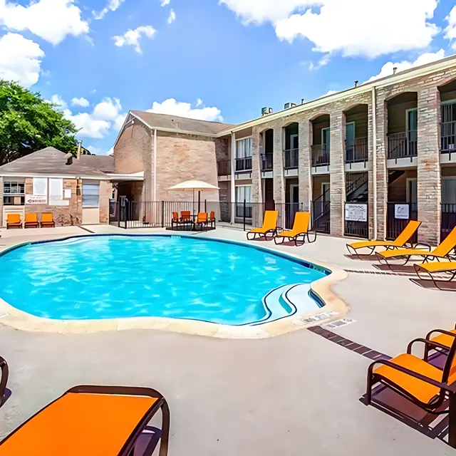 A view of a swimming pool surrounded by orange lounge chairs at an apartment complex.