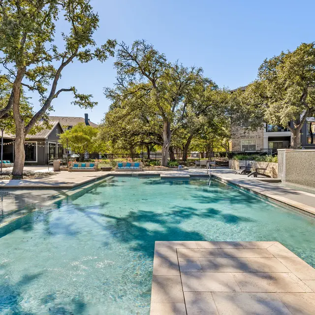 A serene pool area surrounded by trees, with lounge chairs and clear blue water under a bright sky.