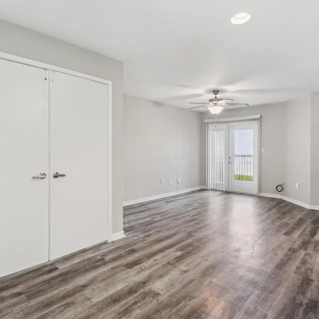 A spacious room with gray walls, hardwood flooring, a ceiling fan, and sliding glass doors leading to an outdoor area.