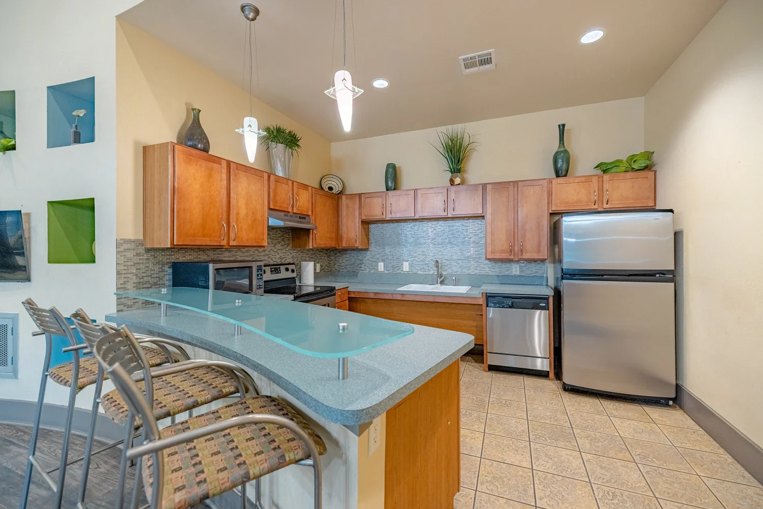 A spacious modern kitchen featuring wooden cabinets, stainless steel appliances, and a large countertop with bar stools.