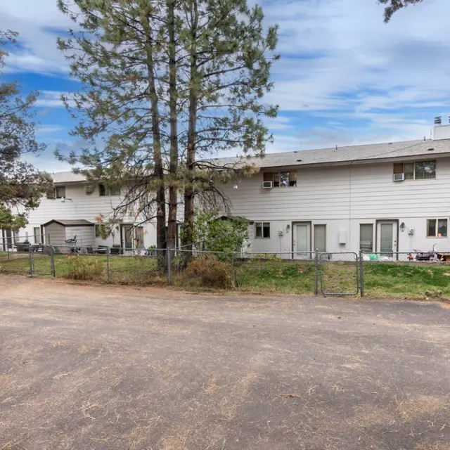 Exterior view of a two-story townhouse complex with a fenced courtyard and surrounding trees.