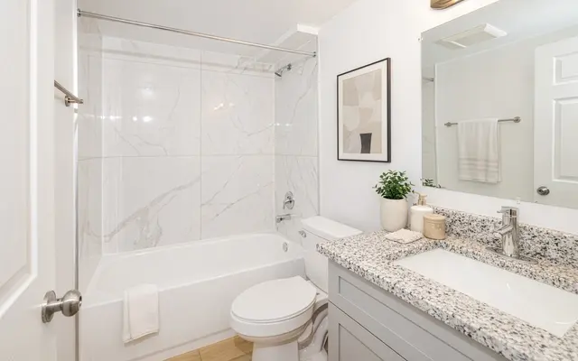 Contemporary Bathroom Interior A clean and modern bathroom featuring a bathtub with a clear shower screen, marble-patterned walls, a large mirror with soft lighting, a sleek sink with a granite countertop, and tasteful decor including a plant and toiletries.