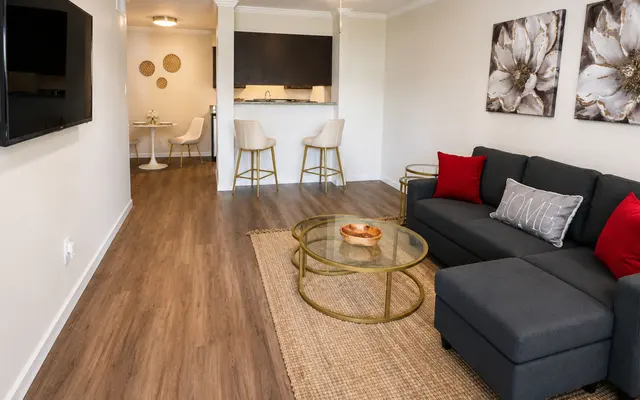 Modern Living Room Interior A modern living room featuring a dark gray sofa with red accent pillows, a glass coffee table, and decorative wall art. The space includes a dining area with white chairs and a bar counter in the background.