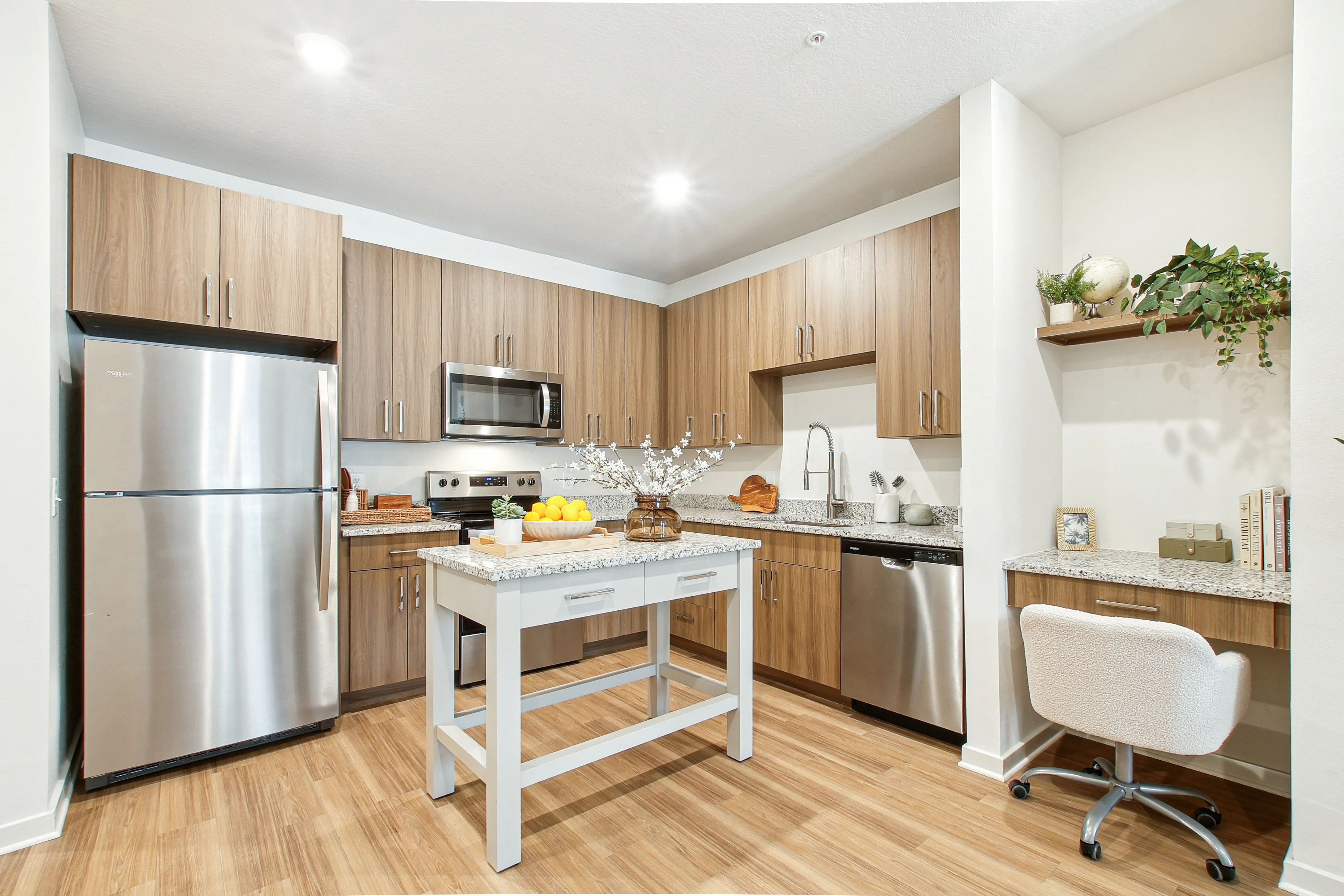 Sundance Trails Modern kitchen with stainless steel appliances, wooden cabinets, a central island, and a small desk area. Bright and inviting design.