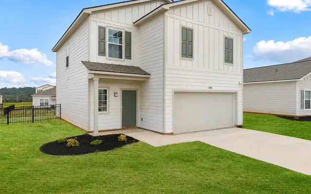 A modern two-story white house with a garage, set in a grassy yard under a blue sky with clouds.