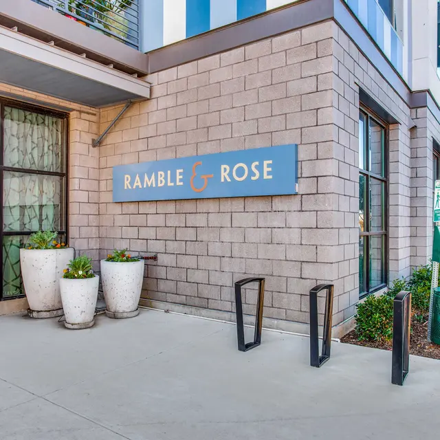 Exterior view of a building with a sign that reads 'Ramble & Rose', and decorative flower pots.