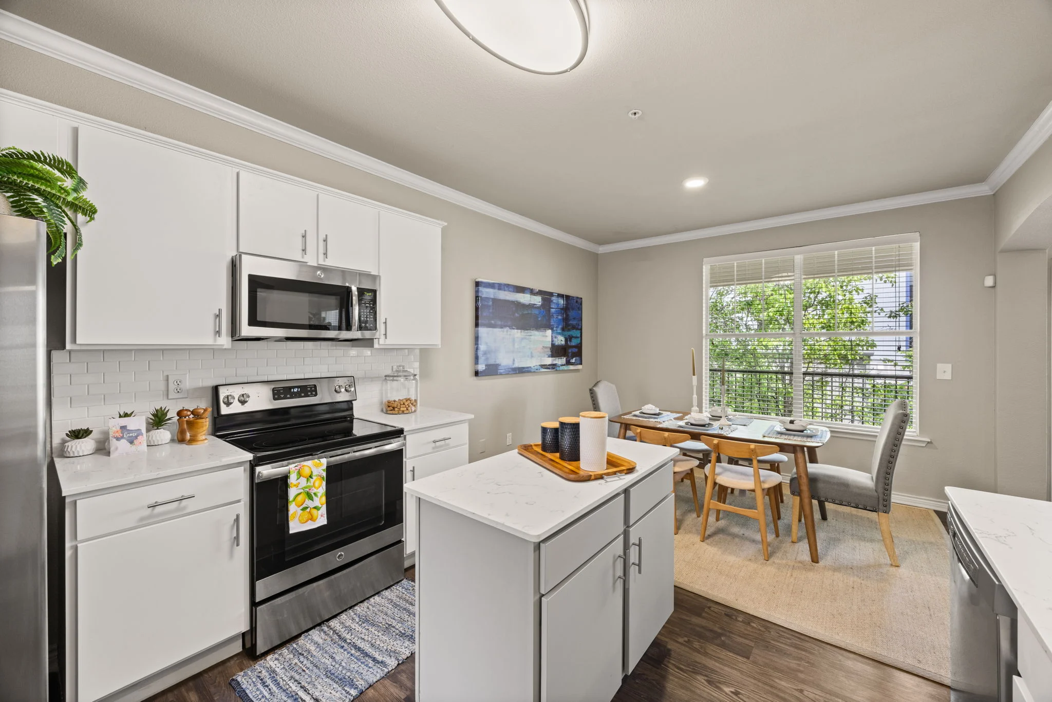 Modern Kitchen and Dining Area A modern kitchen featuring white cabinets, stainless steel appliances, and a dining area with a table and chairs. Natural light enters through the window, and a small island is visible in the center.