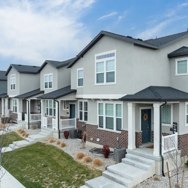 A row of modern townhouses with gray and white facades, small porches, and landscaped yards