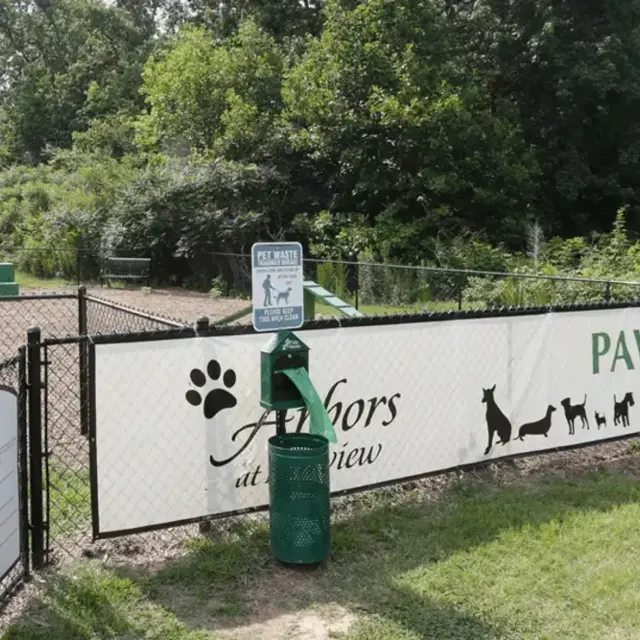 A fenced area designated as Paw Park with green grass, a waste disposal station, and informational signs about park rules.