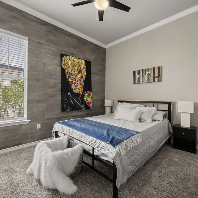 Modern Bedroom Design A modern bedroom featuring a queen-sized bed with grey blankets, a decorative wall art above the bed, and a large window letting in natural light. Soft carpet flooring and neutral wall colors enhance the room's aesthetic.