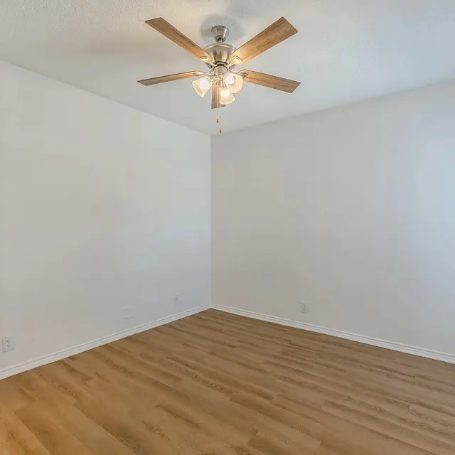An empty room featuring a light-colored wooden floor, a ceiling fan, and a window with blinds.