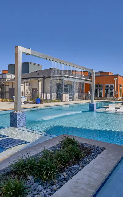 A modern pool area with lounge chairs and a volleyball net, surrounded by landscaped greenery and contemporary buildings.