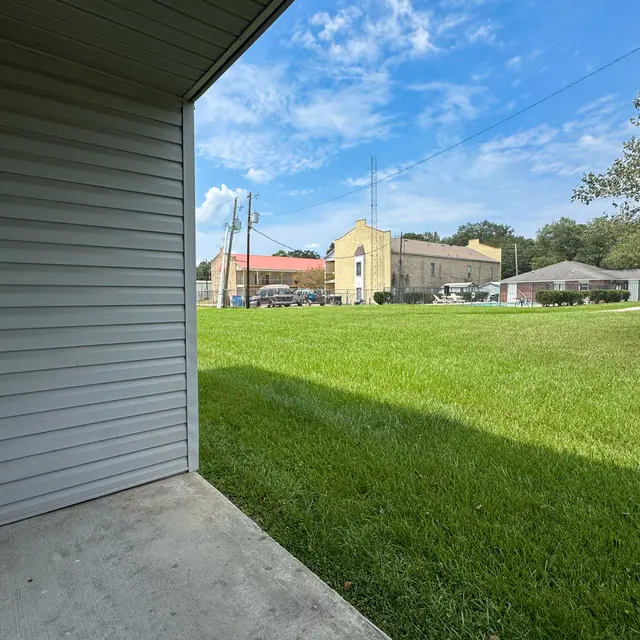 A view from a gray wall corner of a grassy area with two buildings in the background under a partly cloudy sky.