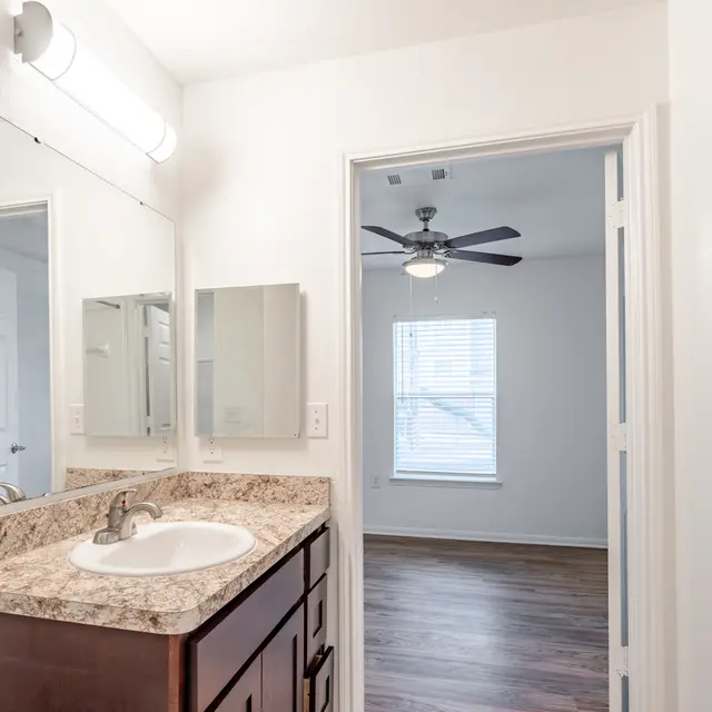 Contemporary Bathroom Interior A modern bathroom featuring a sink with a granite countertop, a large mirror, and light fixtures. The room opens into a light-filled space beyond with a ceiling fan and a window.