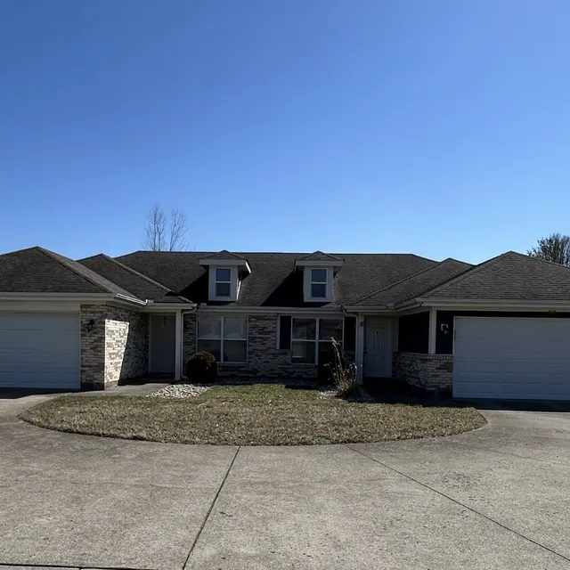 A single-story residential house with a circular driveway, featuring two garages and a well-kept lawn under a clear blue sky.