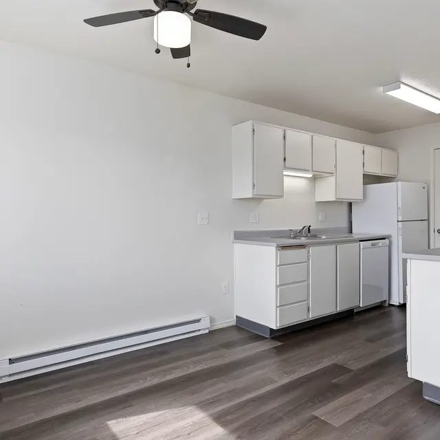 Modern Kitchen Design A modern kitchen with a ceiling fan, white cabinets, and appliances including a refrigerator and microwave. The flooring is dark wood laminate, and the walls are painted white.