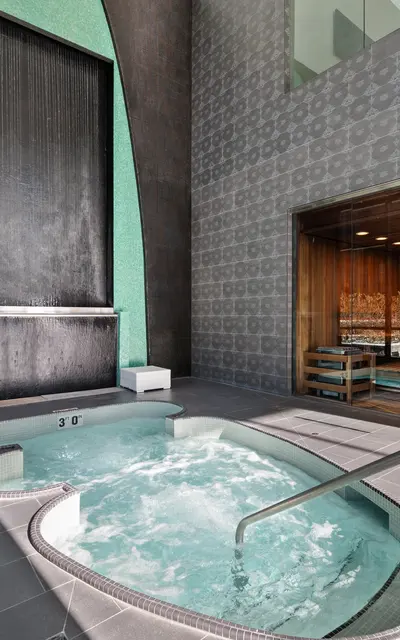 A modern indoor spa area featuring a hot tub and a waterfall wall.