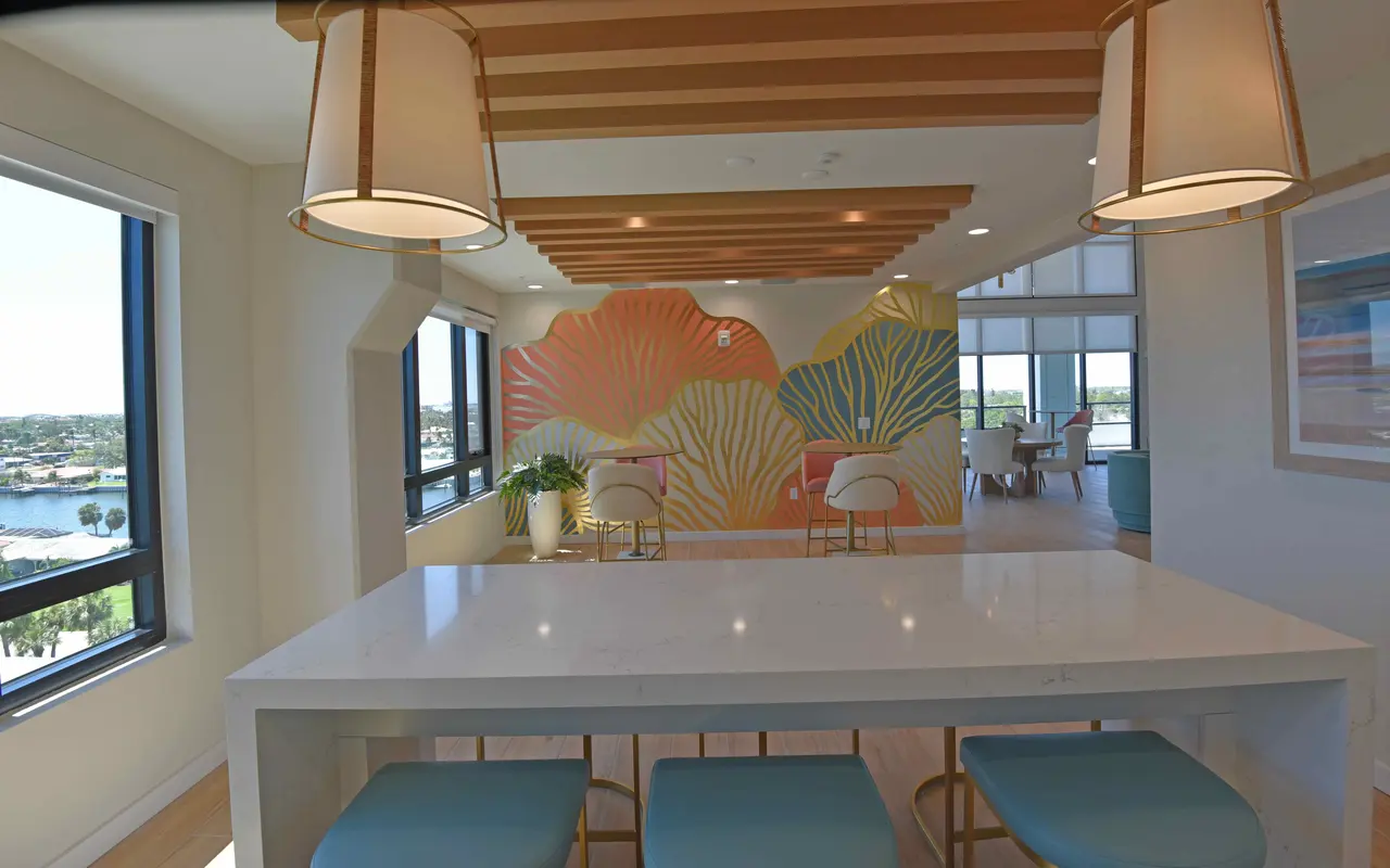 A modern interior space featuring a white table with blue chairs, a colorful coral-inspired mural on the wall, and large windows with a scenic view.