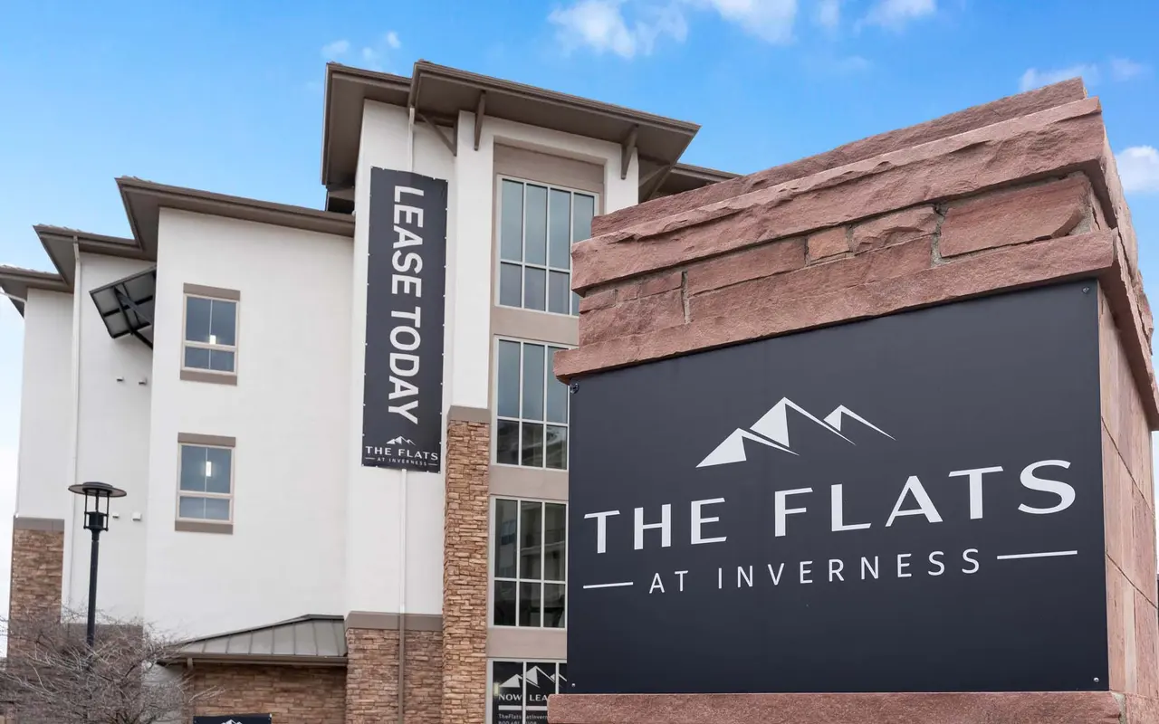 A modern apartment building with a sign that reads 'The Flats at Inverness' and a banner stating 'Lease Today.'