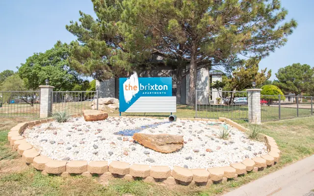 Exterior sign for The Brixton Apartments surrounded by landscaping features including rocks and gravel.