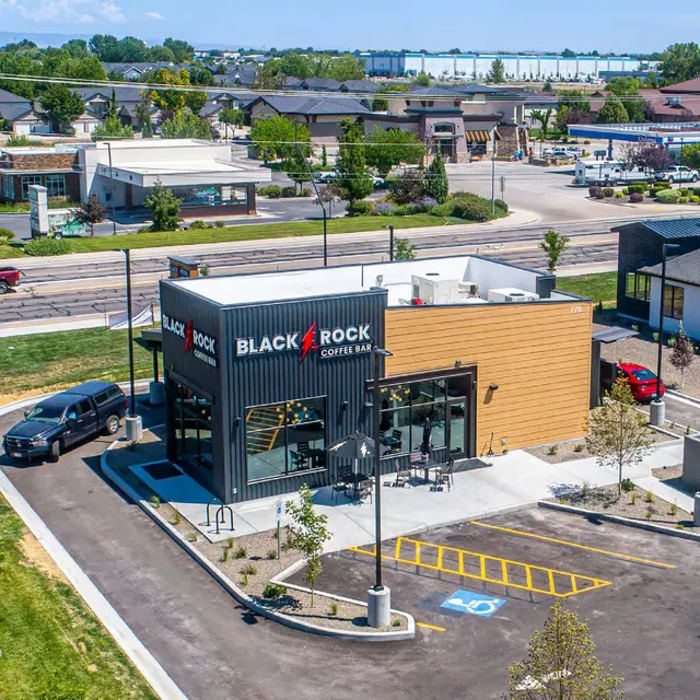 Aerial view of a modern coffee shop named Black Rock Coffee located in a parking lot with nearby buildings and trees.