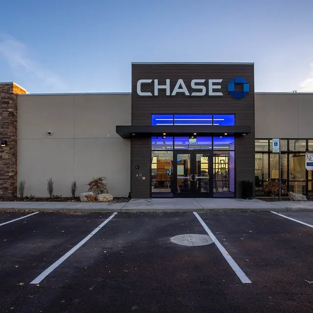 Exterior view of a Chase Bank branch featuring a modern design, with a stone accent wall and blue illuminated signage over the entrance.