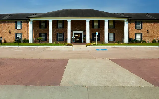 A brick building with white columns, lawn, and parking area in the foreground.