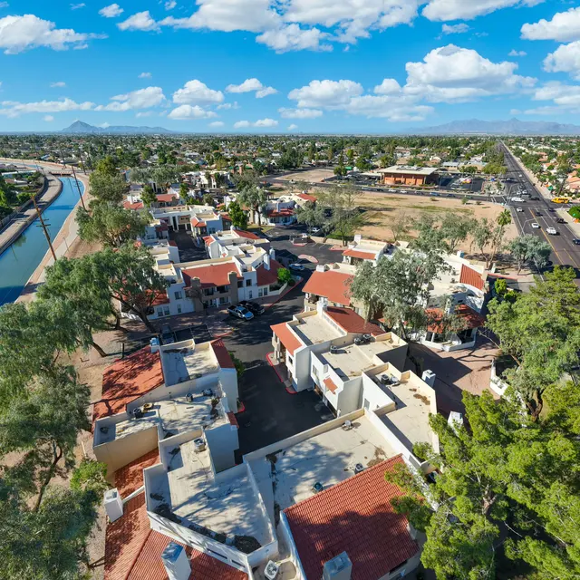 Aerial view of a suburban neighborhood with houses, a canal, and a road in the background under a blue sky with clouds.