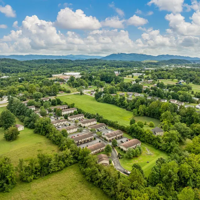 Aerial view of a rural area featuring clusters of homes surrounded by greenery and hills in the background.