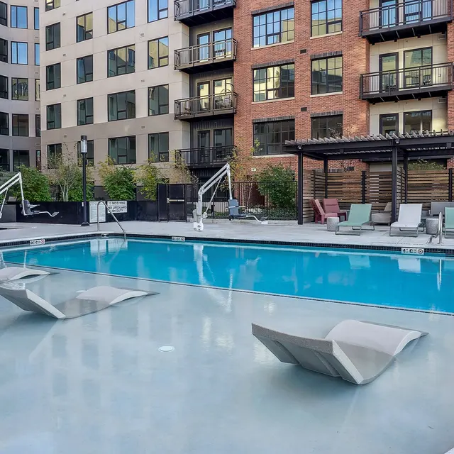 Modern Apartment Pool Area A modern apartment complex featuring a swimming pool surrounded by lounge chairs and greenery.