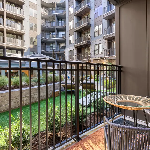 A balcony view overlooking a green courtyard with wooden landscaping and modern apartment buildings in the background.