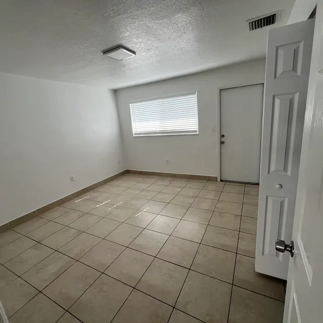 Empty room with white walls, a tiled floor, a window with blinds, and a door partially open on the right side.