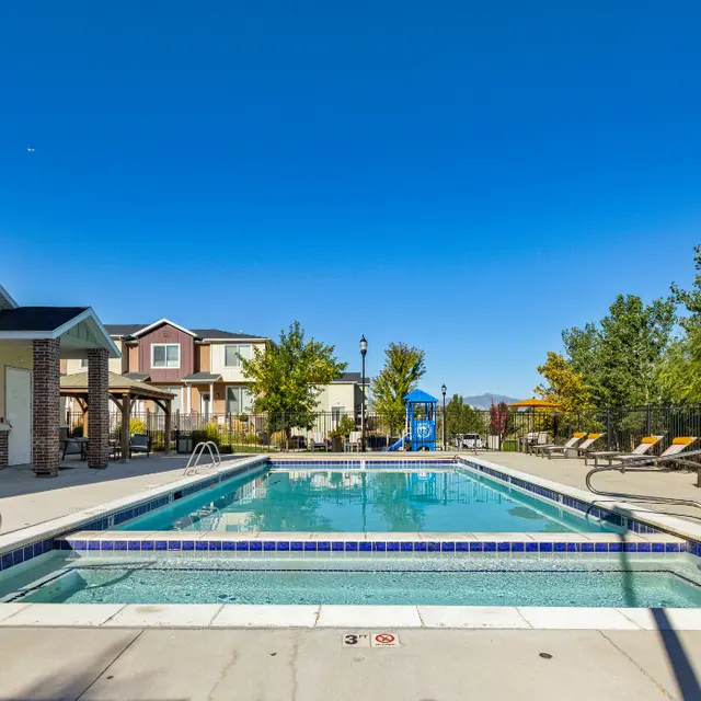 Relaxing Swimming Pool Area A clear swimming pool surrounded by lounge chairs and trees, with a bright blue sky above.
