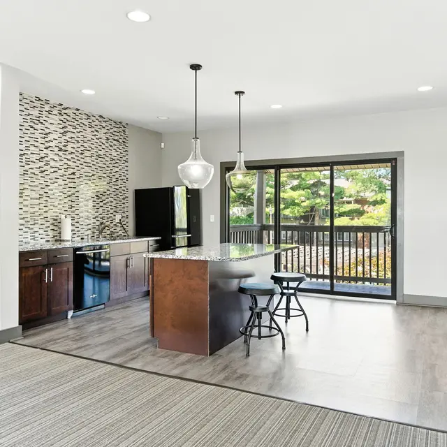 A modern kitchen with dark cabinetry and a countertop island, featuring pendant lighting and a view of a balcony through large glass doors.