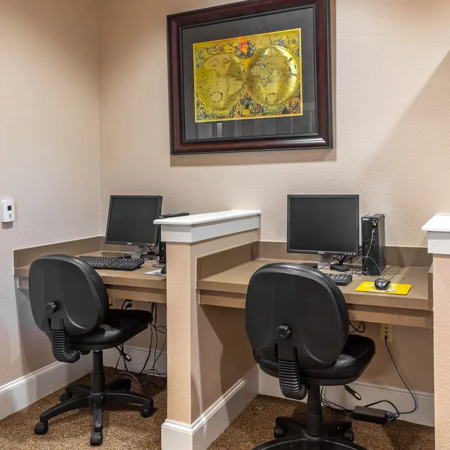 Office Workstations Two workstations with desktop computers and black office chairs situated against a beige wall, featuring framed artwork above.