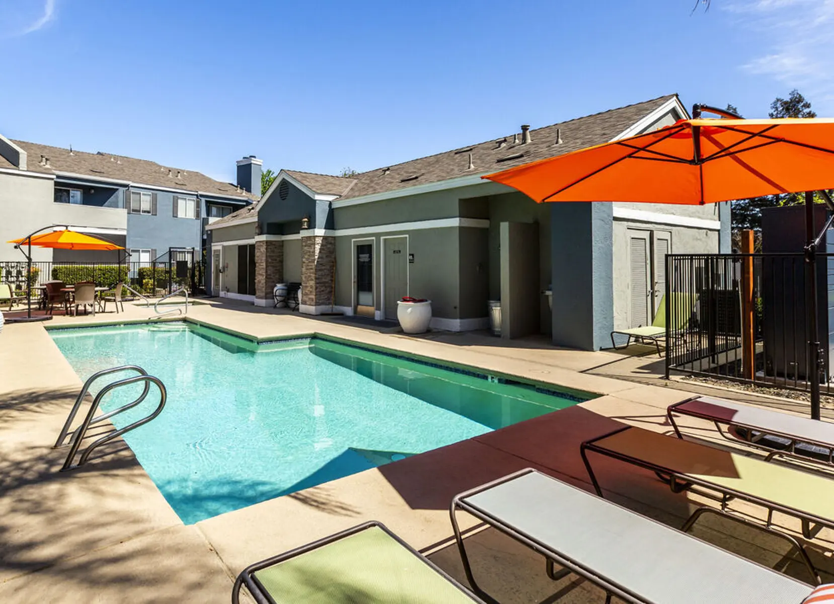 A pool area with lounge chairs and umbrellas, complemented by a clear blue sky and modern architecture in the background.