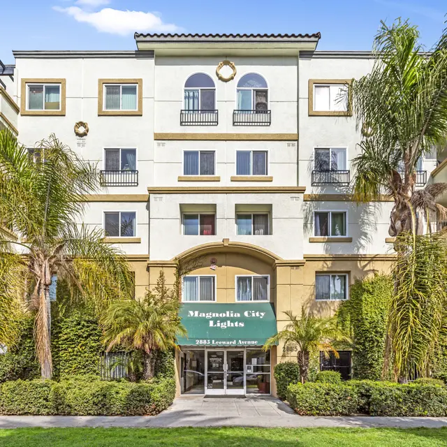 A multi-story residential building named Magnolia City Lights with a green awning. The building features balconies and palm trees in the foreground.