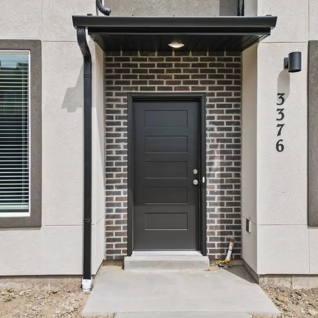 Exterior view of a modern front door area featuring a dark door and brick detailing next to windows.