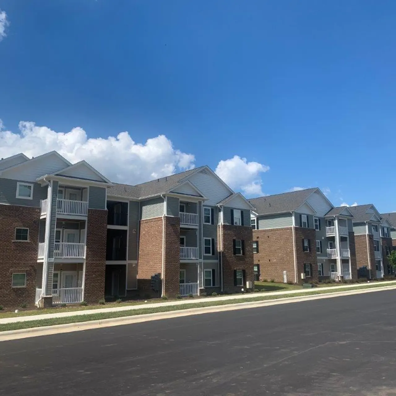 Row of residential apartment buildings with brick and siding exteriors, under a clear blue sky with a few clouds.