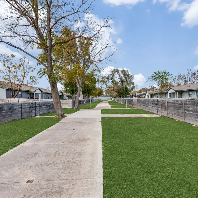 Walking Path Between Houses A clear concrete pathway surrounded by green grass, leading between houses with wooden fencing on either side.