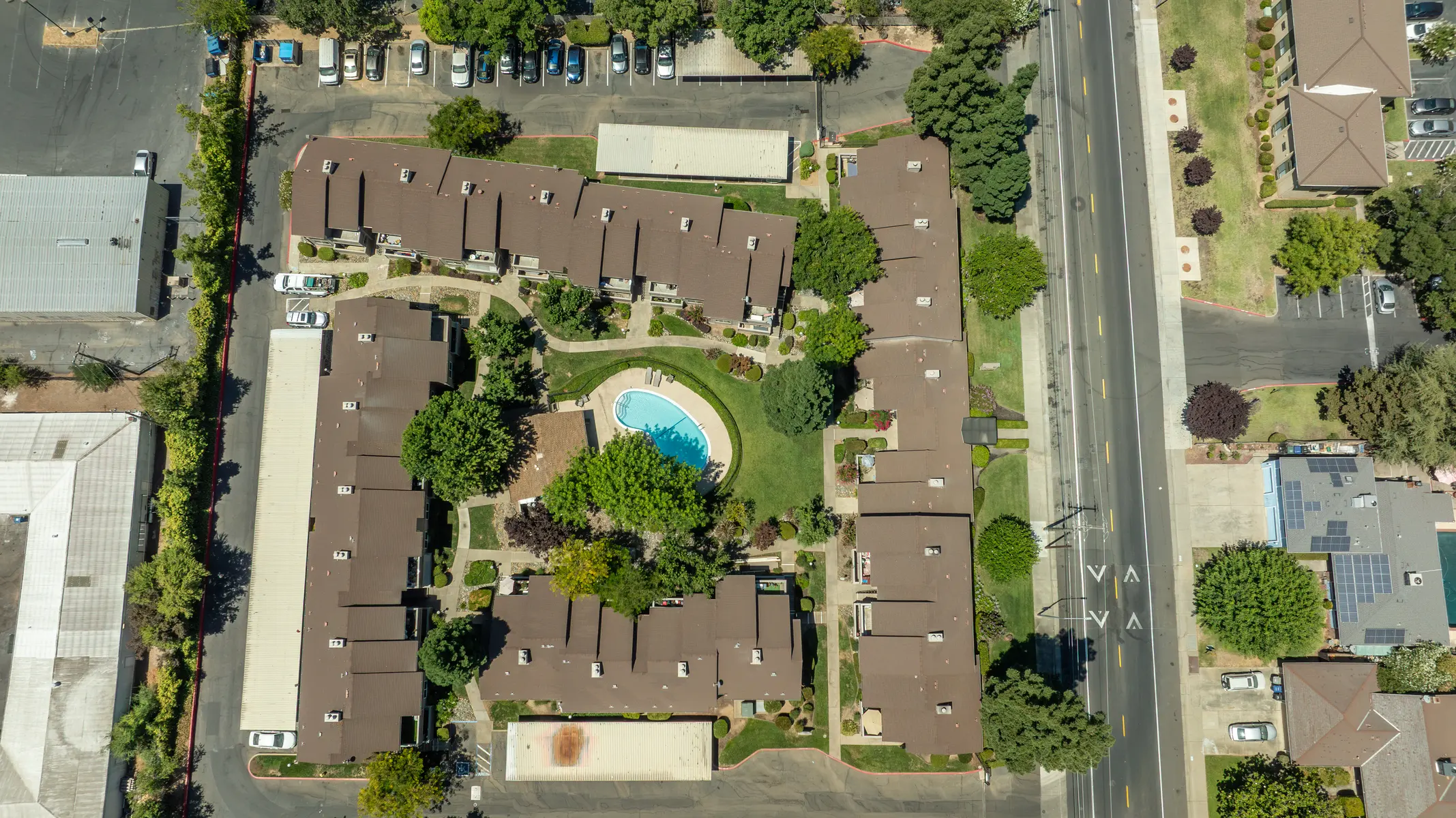 Aerial view of a complex with several buildings surrounding a pool and landscaped areas.