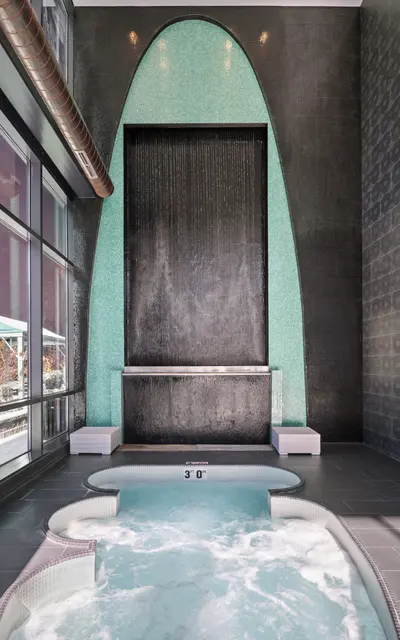 A modern spa area featuring a sleek wall with a waterfall, surrounded by turquoise tiles and a hot tub with bubbling water.