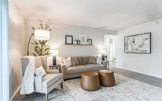 Cozy living room with a grey sofa, patterned armchair, two brown coffee tables, and decorative wall art. Bright and airy atmosphere.