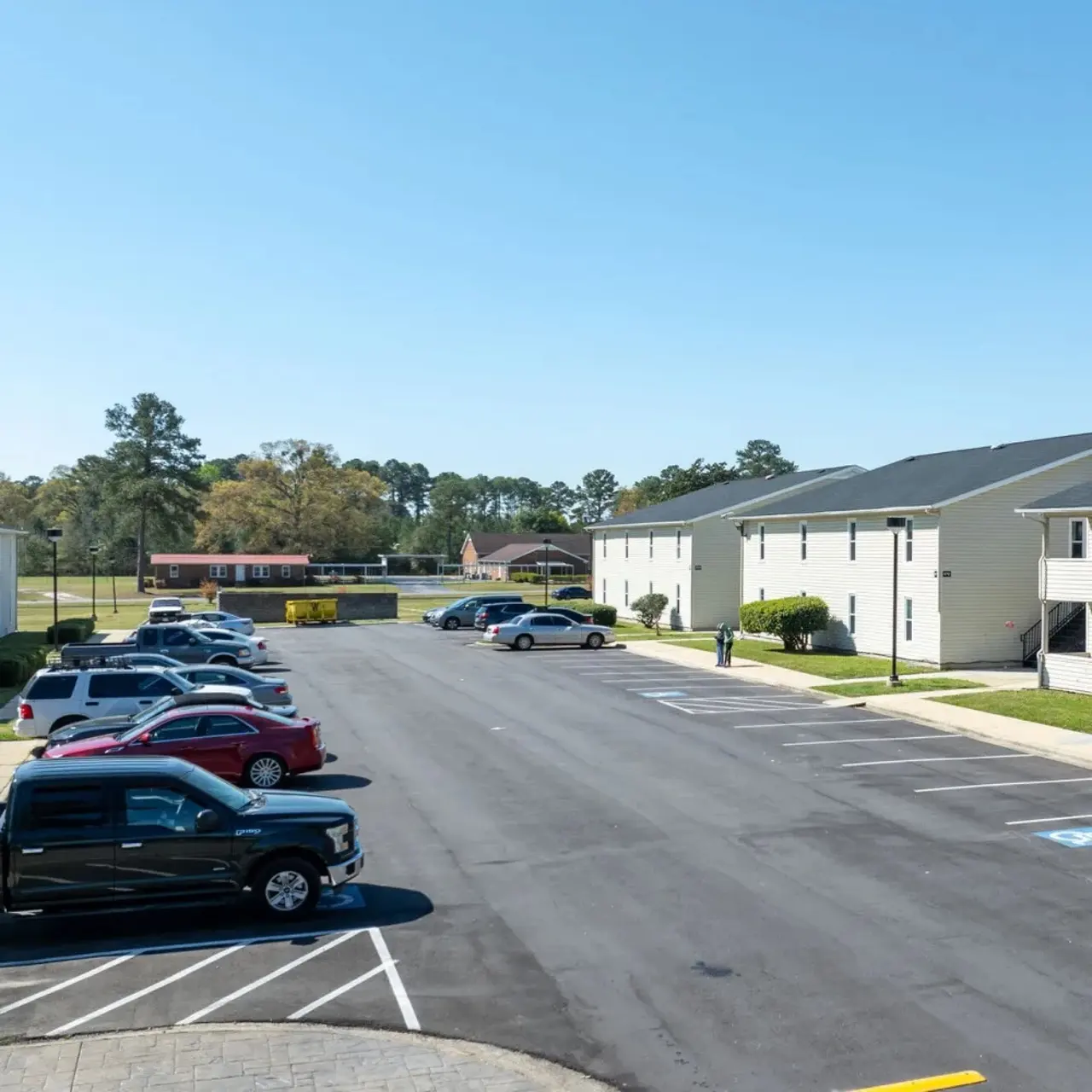 A view of a parking lot in an apartment complex with several cars parked in various spots and residential buildings in the background.