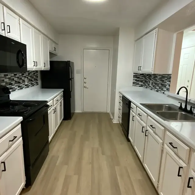 A modern kitchen featuring white cabinets, black appliances, and a light-colored countertop. The backsplash has a geometric design in gray and black. The kitchen is well-lit and has an open layout.