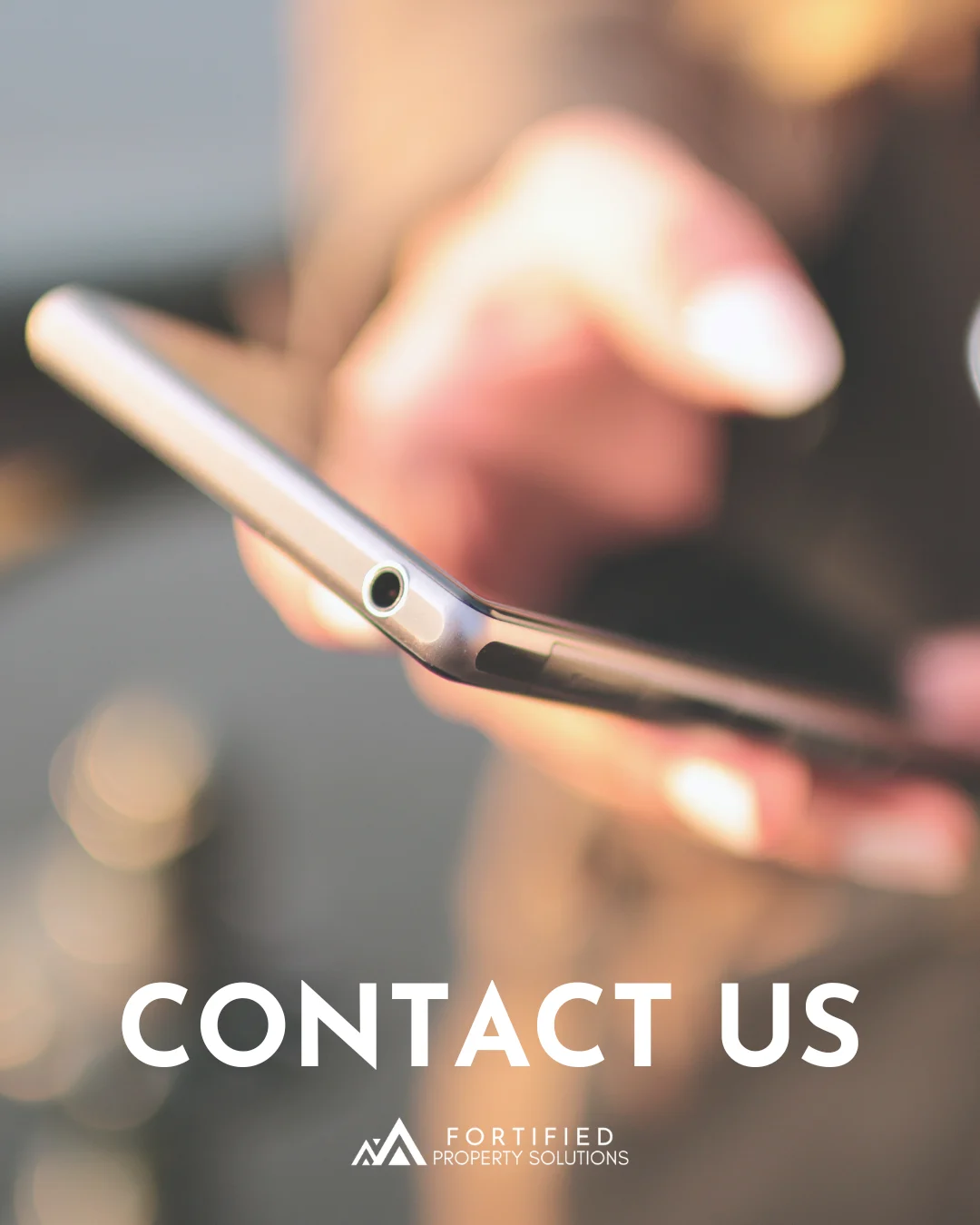 Contact Us - Fortified Property Solutions A close-up of a hand holding a smartphone with a blurred background. The text 'CONTACT US' is prominently displayed at the bottom.