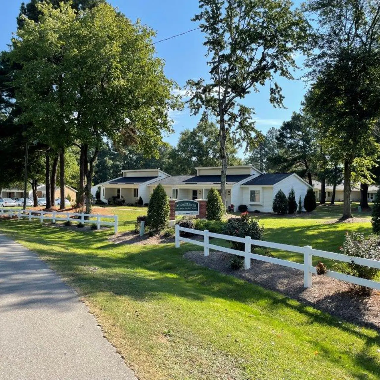 A scenic view of suburban homes with trees and a white fence.